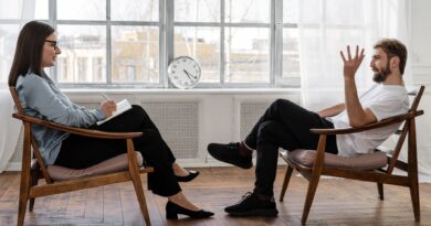 person in black pants and black shoes sitting on brown wooden chair